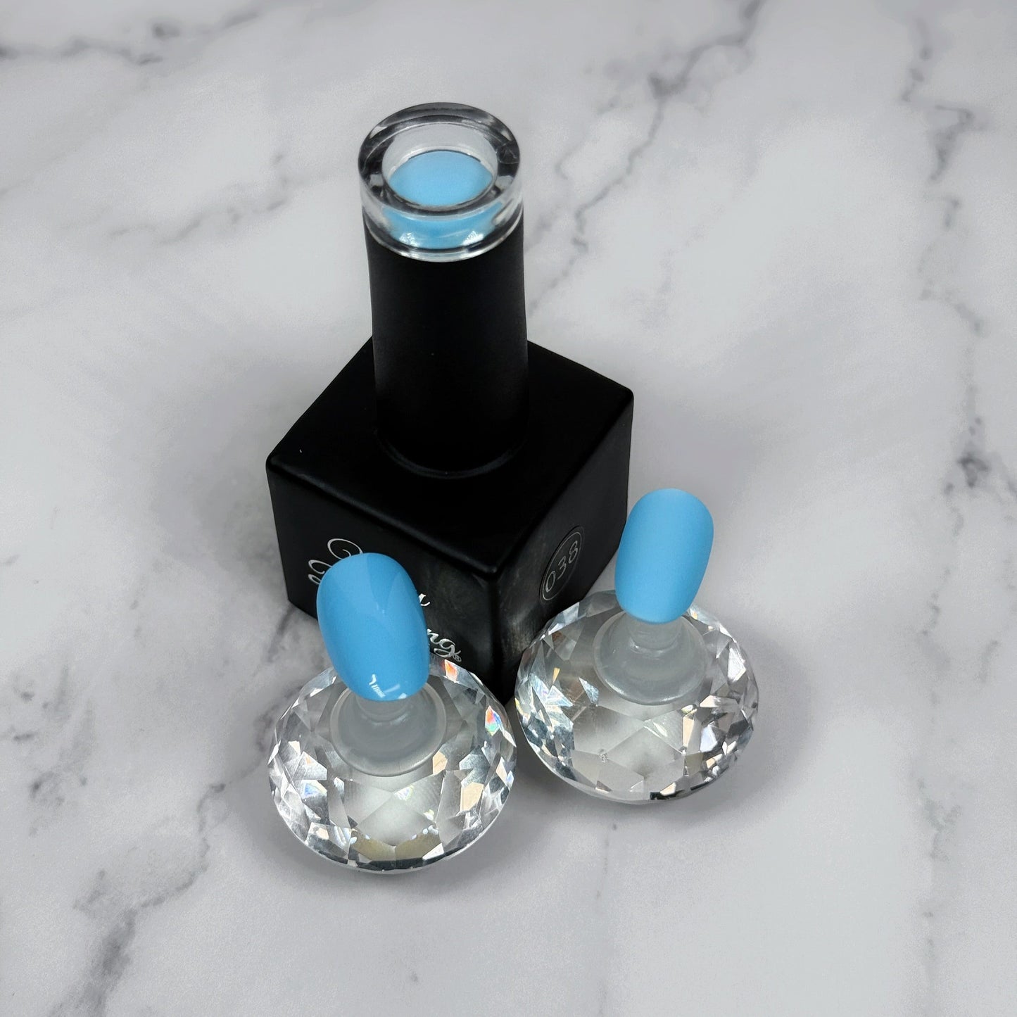 Nail polish bottle with two sample nails showing light blue polish with matte and glossy topcoat