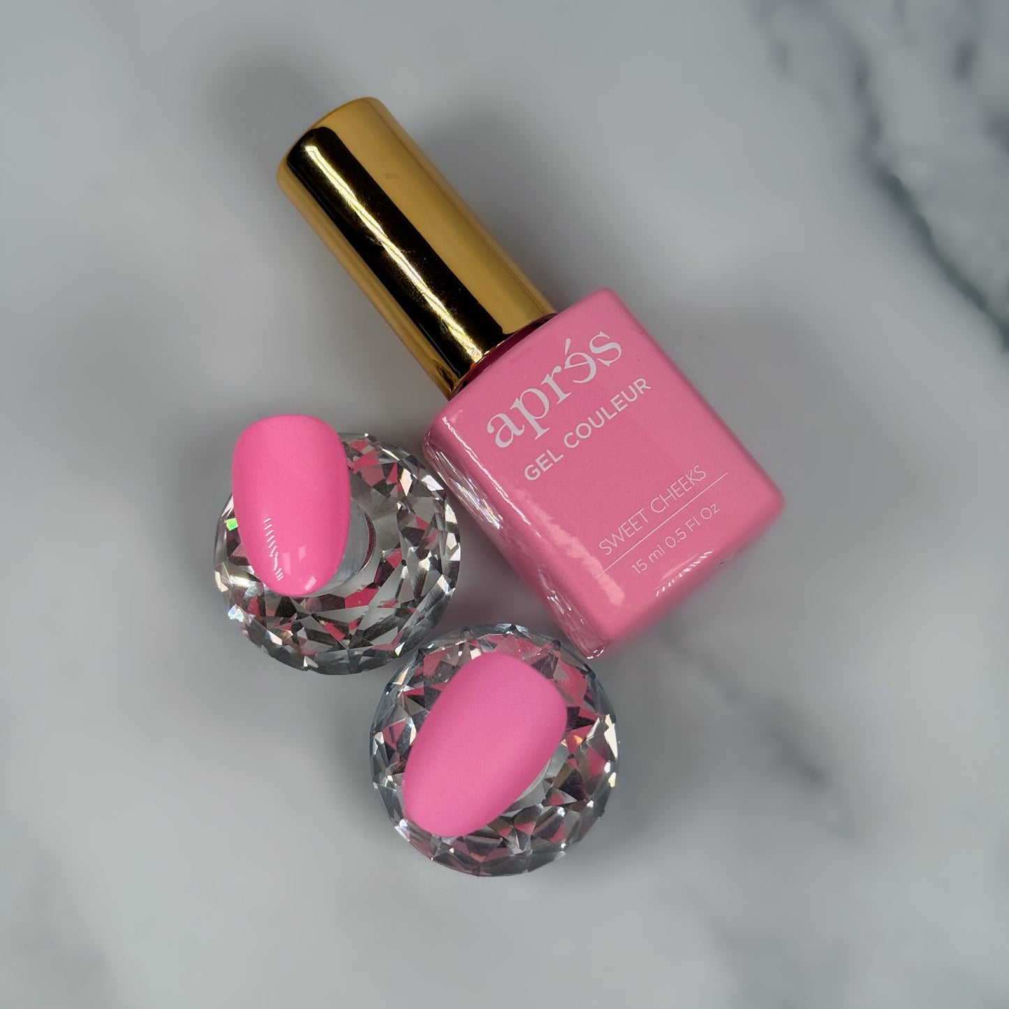 Pink nail polish bottle with a gold cap on a marble surface with two sample nails showing a matte versus glossy topcoat