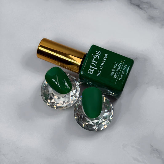 Green nail polish bottle with two green nail samples showing matte and glossy topcoat on a marble surface