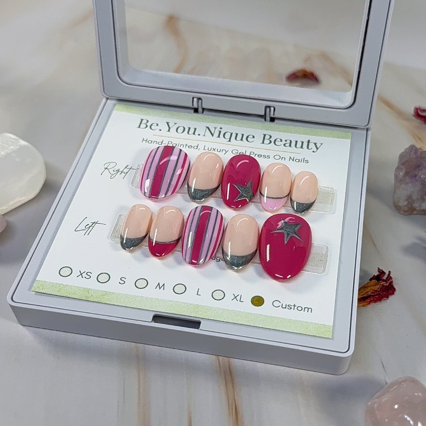 Set of reusable custom press on nails on a short almond nail. two tone pink with stripes and silver accents, pink and silver french tips and silver start accents.