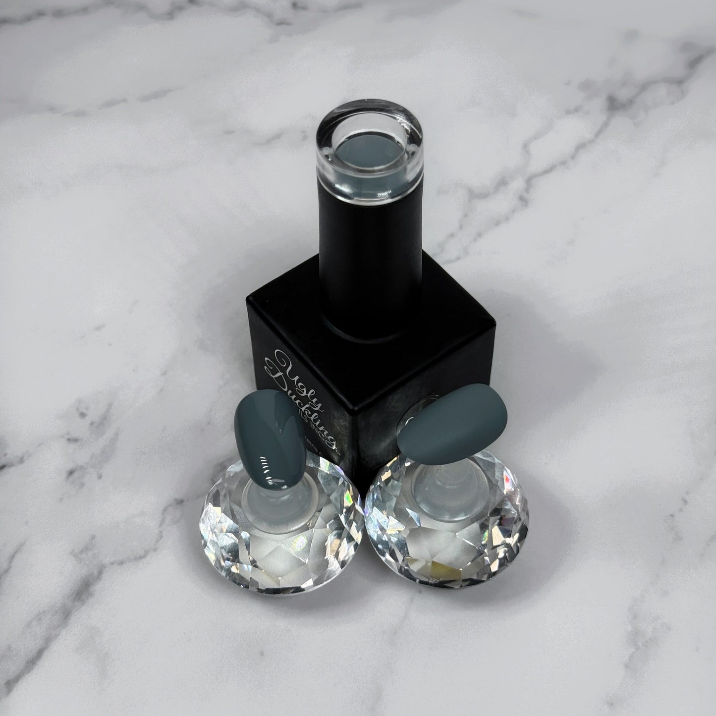 nail polish bottle with two sample nails showing a medium grey colour and what they look like with glossy vs matte topcoat