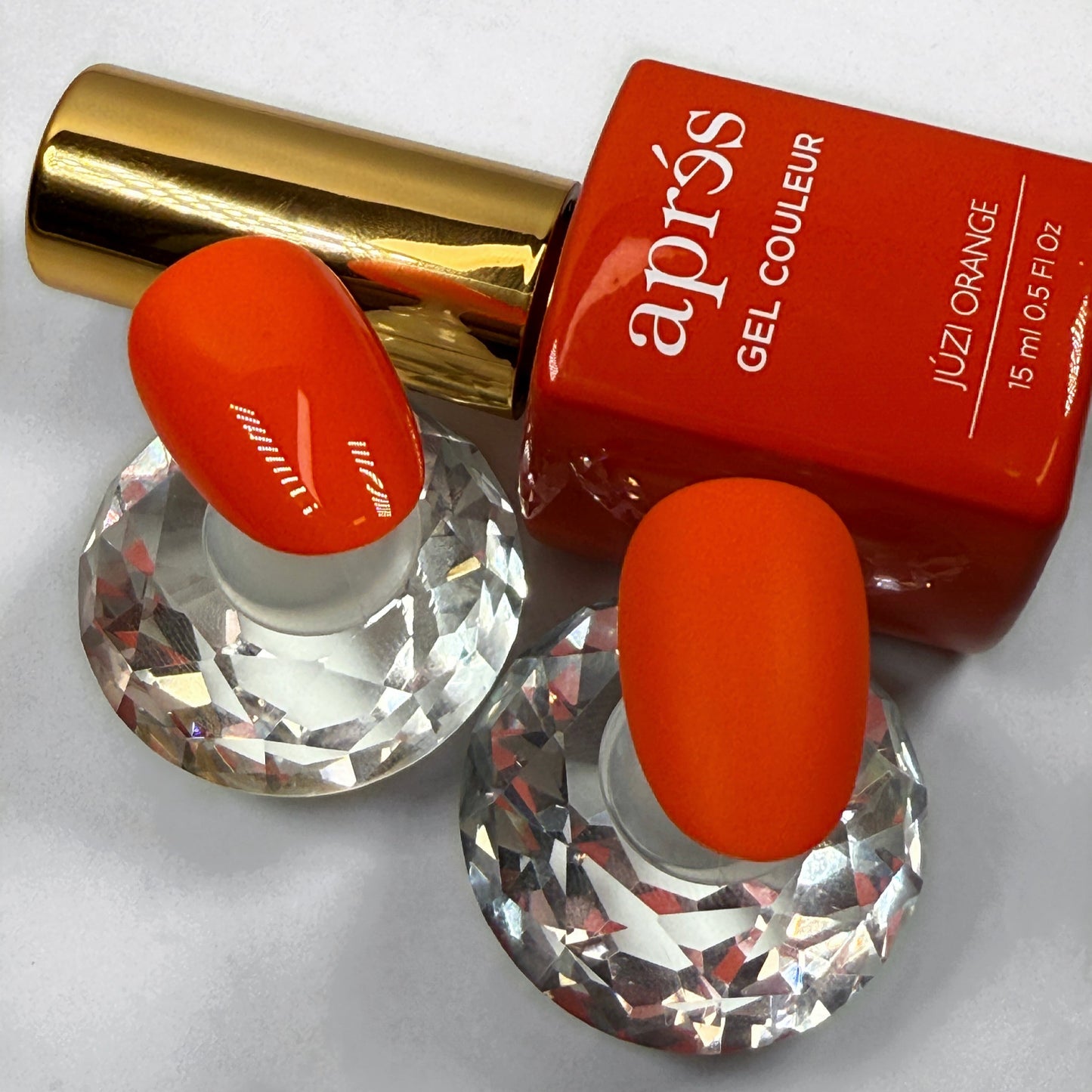 Orange nail polish bottle with gold cap and two sample nails showing the colour with matte versus glossy topcoat on a white background