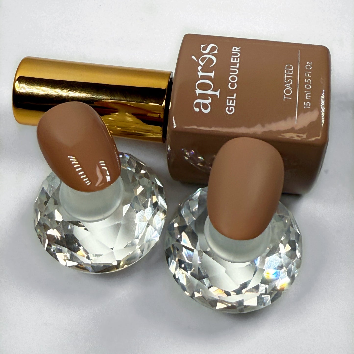 Apres Toasted nail polish bottle with two nail samples showing the polish with matte and glossy topcoat on a white background