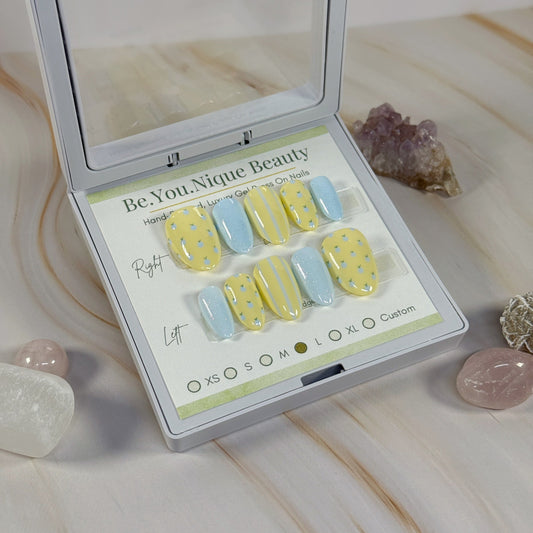 Set of yellow and blue nail art samples in a 'Be You Nique Beauty' case on a light marble surface.