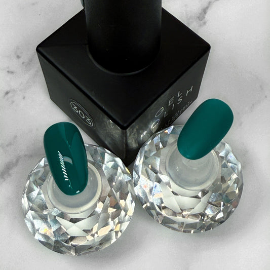 Teal nail polish bottle with two matching nail samples showing a gloss and matte topcoat option on a marble background