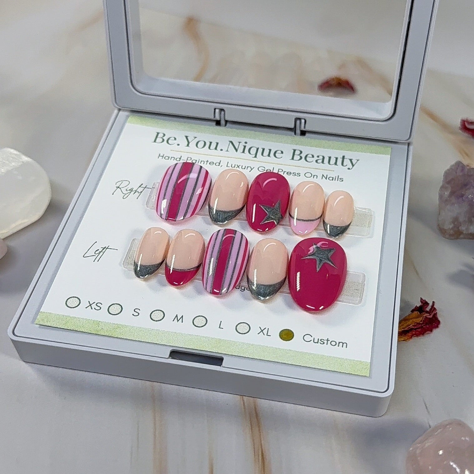 Set of reusable custom press on nails on a short almond nail. two tone pink with stripes and silver accents, pink and silver french tips and silver start accents. 