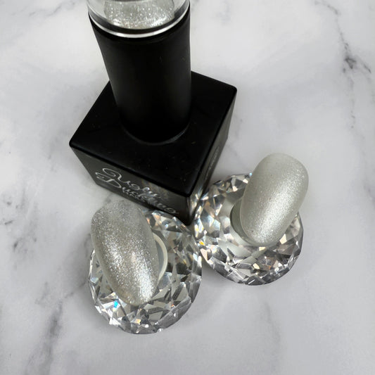 black nail polish bottle with two sample nails showing a shimmery white polish with a glossy and matte topcoat on a marble background