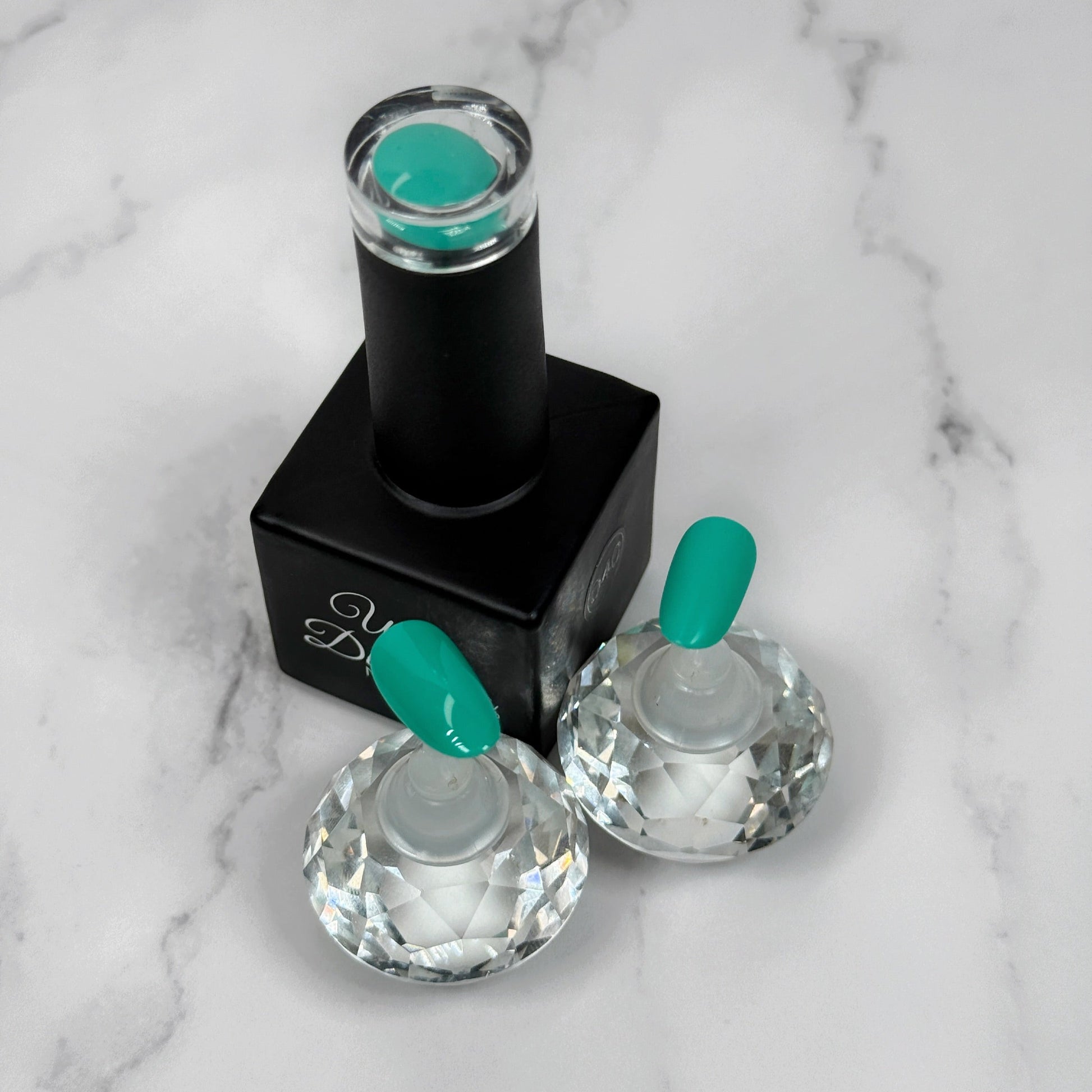 Nail polish bottle with turquoise nail tips showing the colour with a matte versus a glossy topcoat on a marble surface