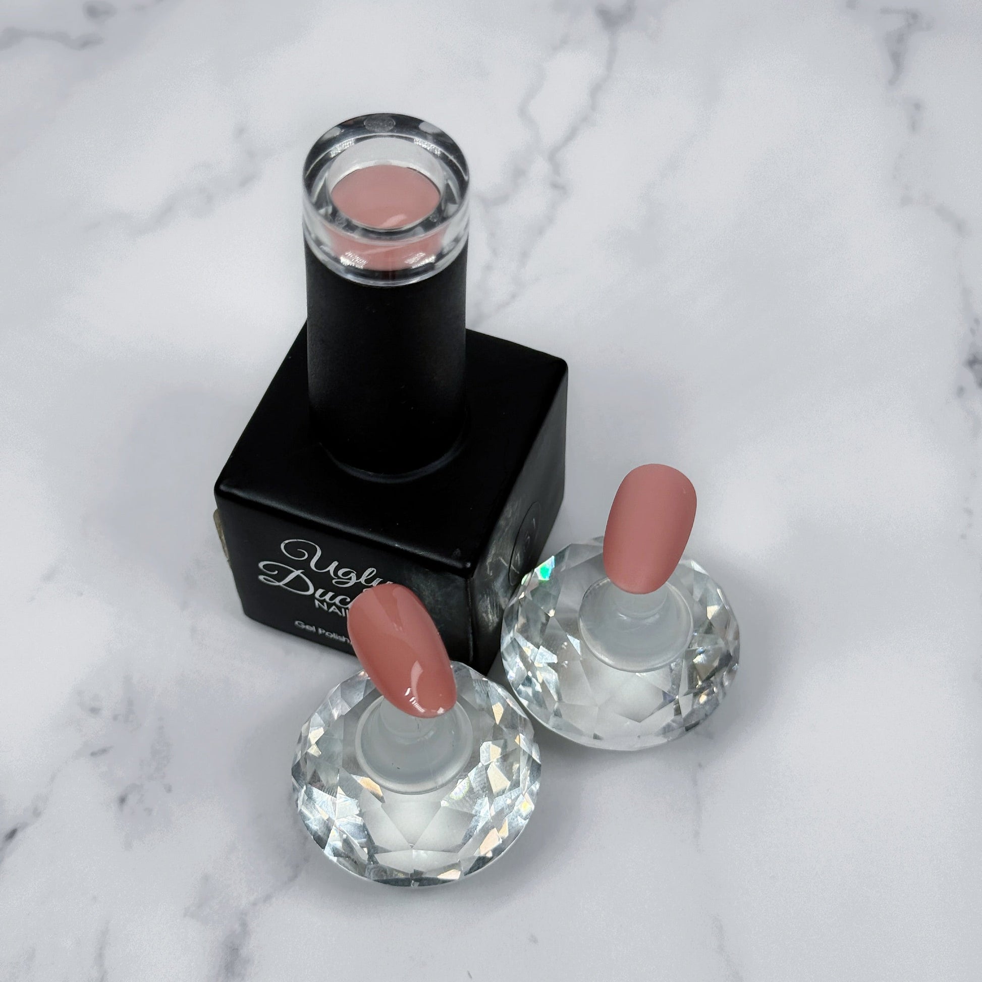 Nail polish bottle with pink top and two sample nails showing the colour with a matte and glossy topcoat on a marble surface.