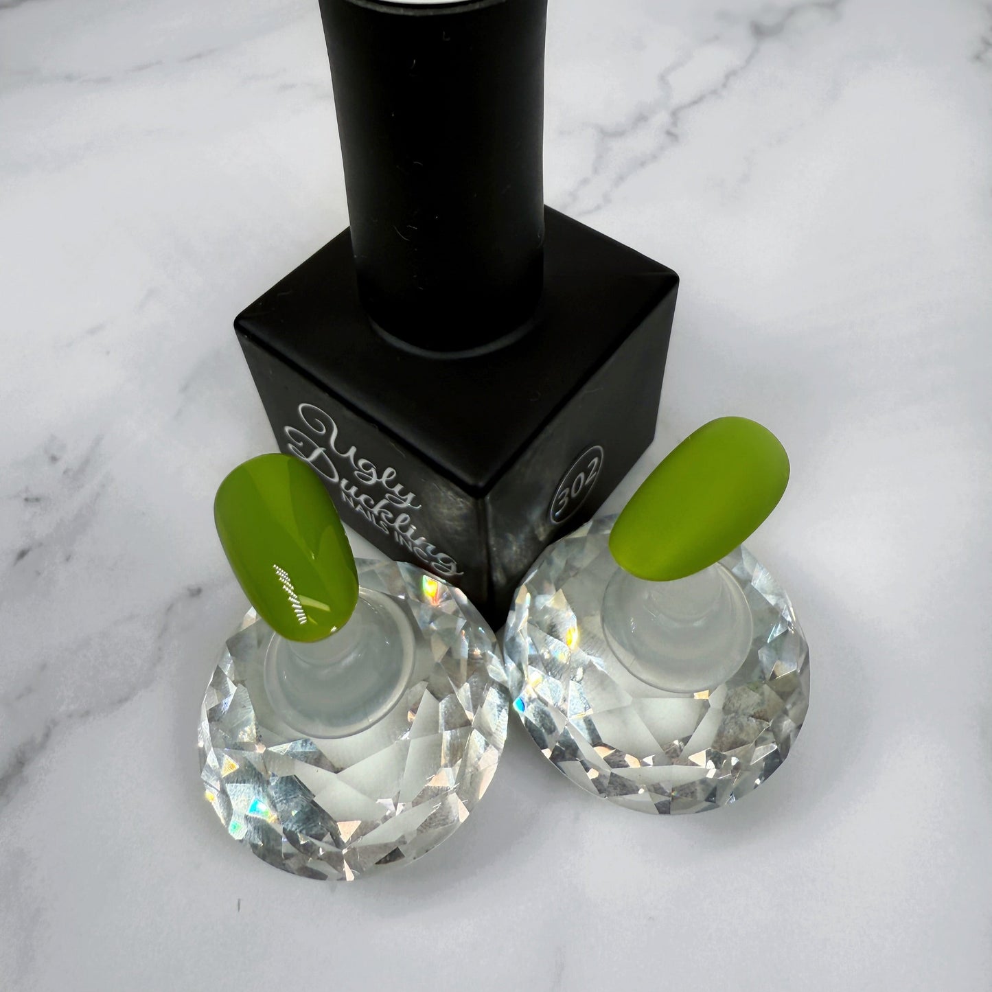 A nail polish bottle with two sample nails showcasing the bright green colour with a matte and glossy topcoat.