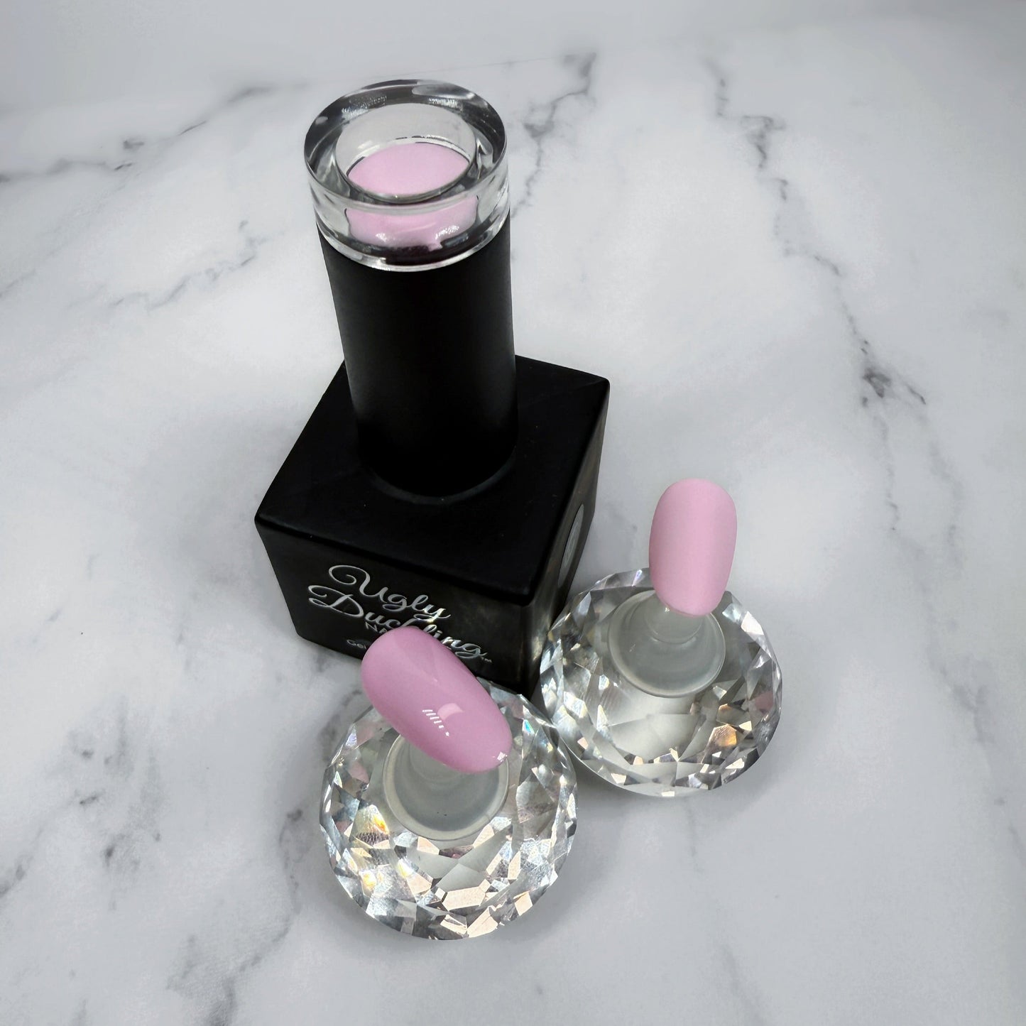 Nail polish bottle with pink top and two sample nails showing the colour with a matte and glossy topcoat on a marble surface.