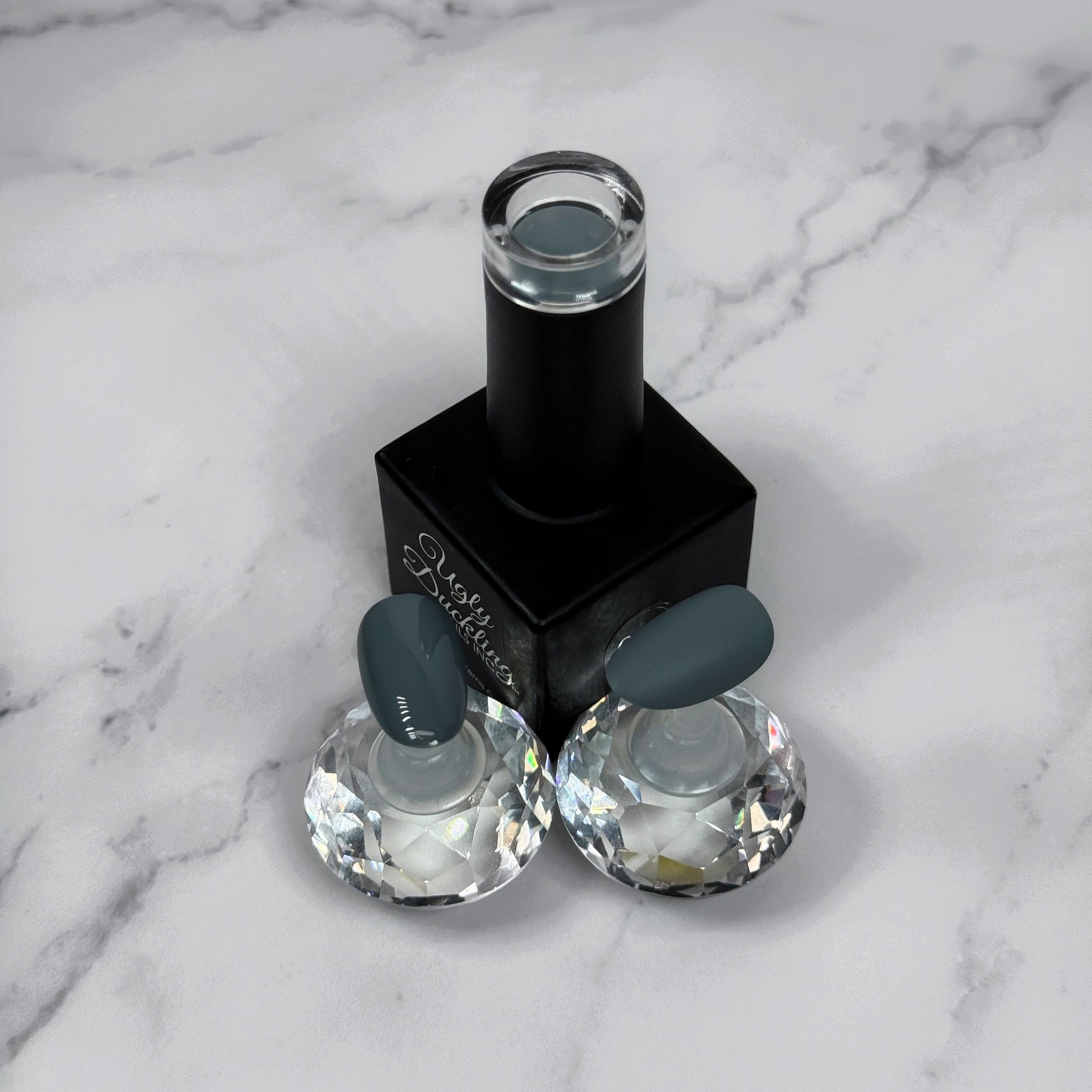 nail polish bottle with two sample nails showing a medium grey colour and what they look like with glossy vs matte topcoat 
