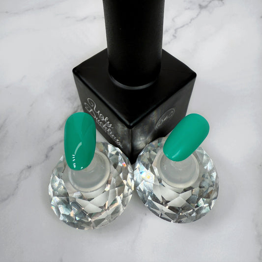 a nail polish bottle with two nail tips showcasing a light teal colour, the two nails show the difference between matte and glossy topcoats.