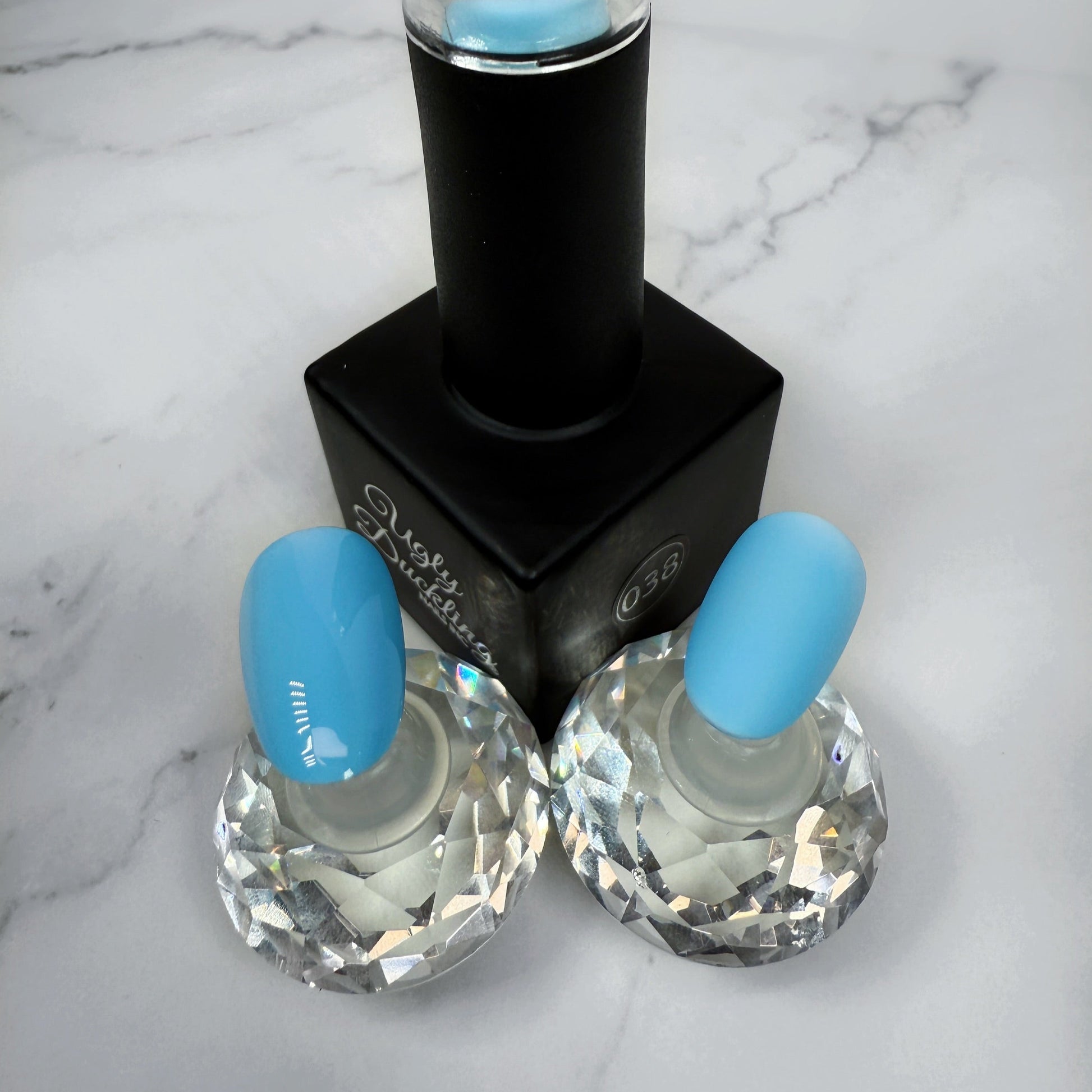 Nail polish bottle with two sample nails showing light blue polish with matte and glossy topcoat