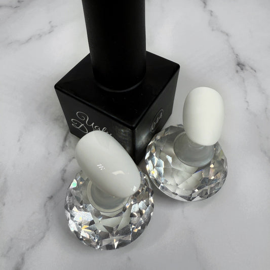 Black nail polish bottle with two nail samples showing glossy and matte topcoat on a marble surface