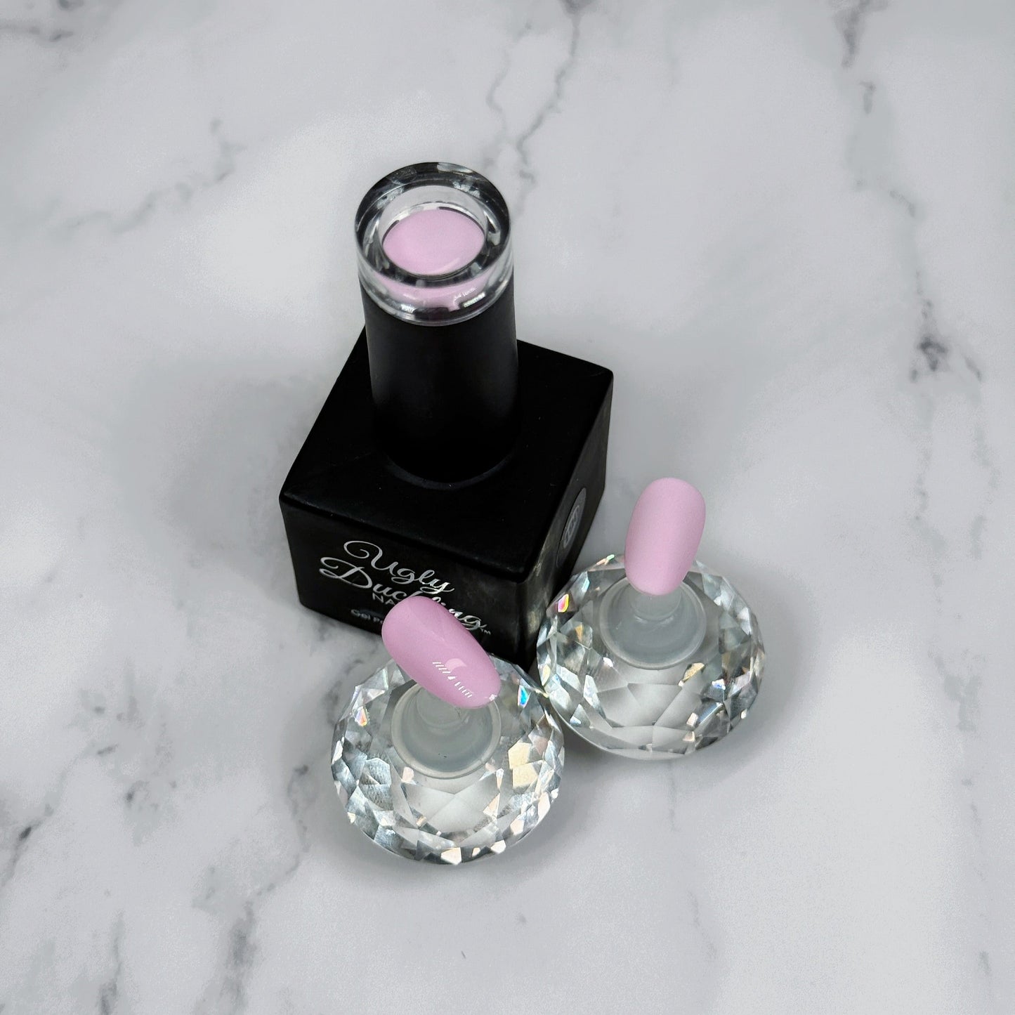 Nail polish bottle with pink top and two sample nails showing the colour with a matte and glossy topcoat on a marble surface.