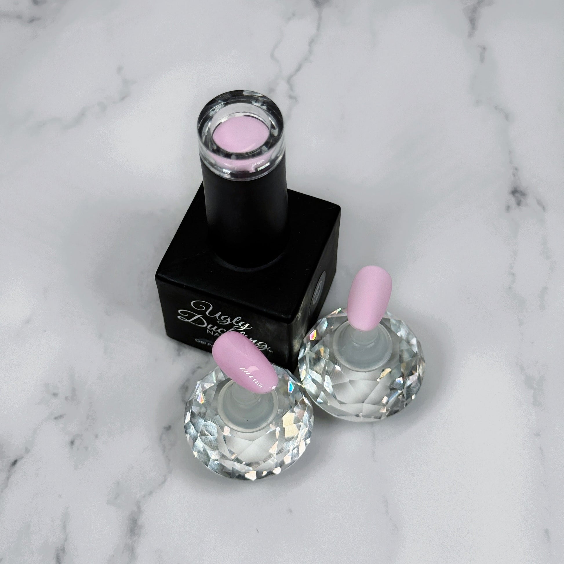 Nail polish bottle with pink top and two sample nails showing the colour with a matte and glossy topcoat on a marble surface.