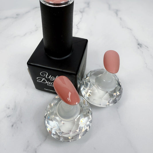Nail polish bottle with pink top and two sample nails showing the colour with a matte and glossy topcoat on a marble surface.