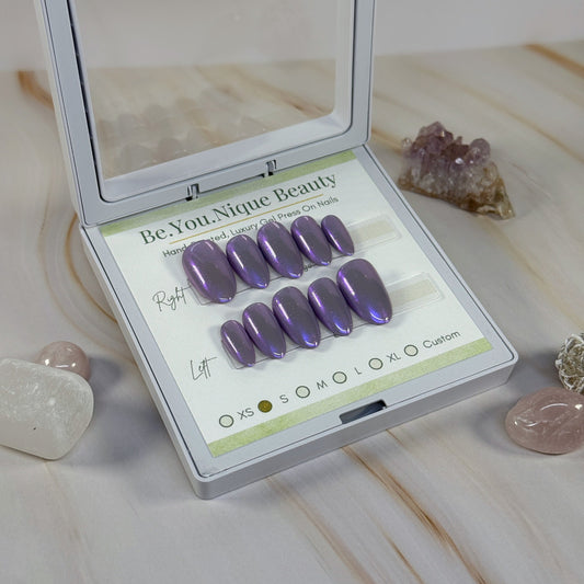 Set of purple chrome press on nails in a Be.You.Nique Beauty case on a marble surface with crystals.