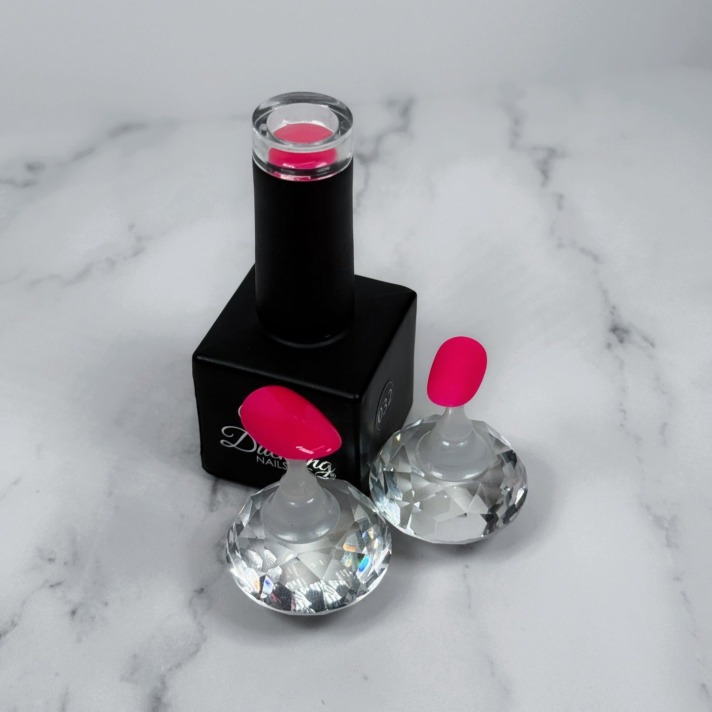 Black nail polish bottle with pink cap and two sample nails with glossy and matte topcoats on a marble surface