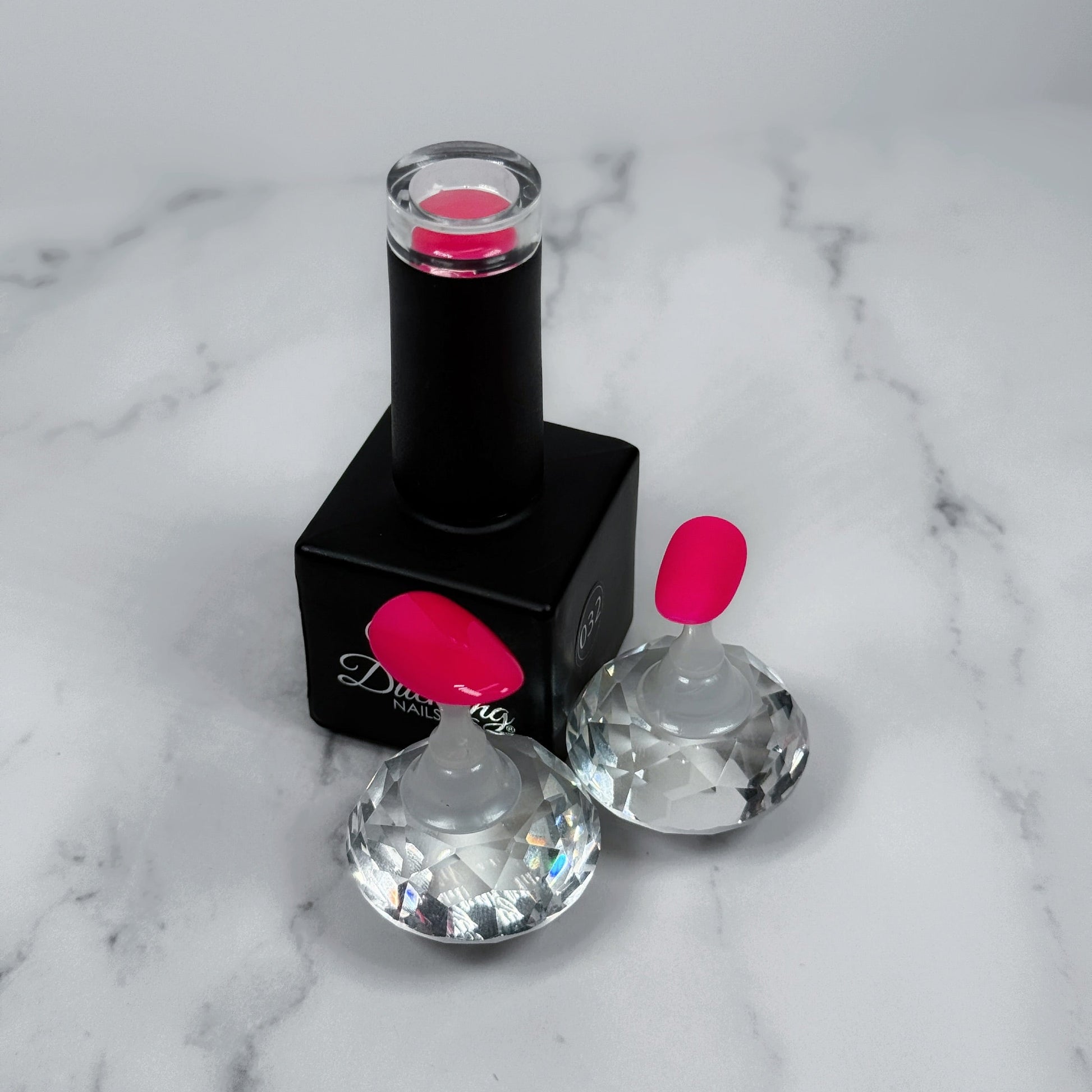 Black nail polish bottle with pink cap and two sample nails with glossy and matte topcoats on a marble surface