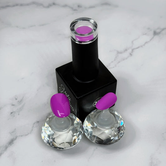 A nail polish bottle with a pink/purple cap and two sample nails showcasing the polish with a glossy and matte topcoat on a marble surface.