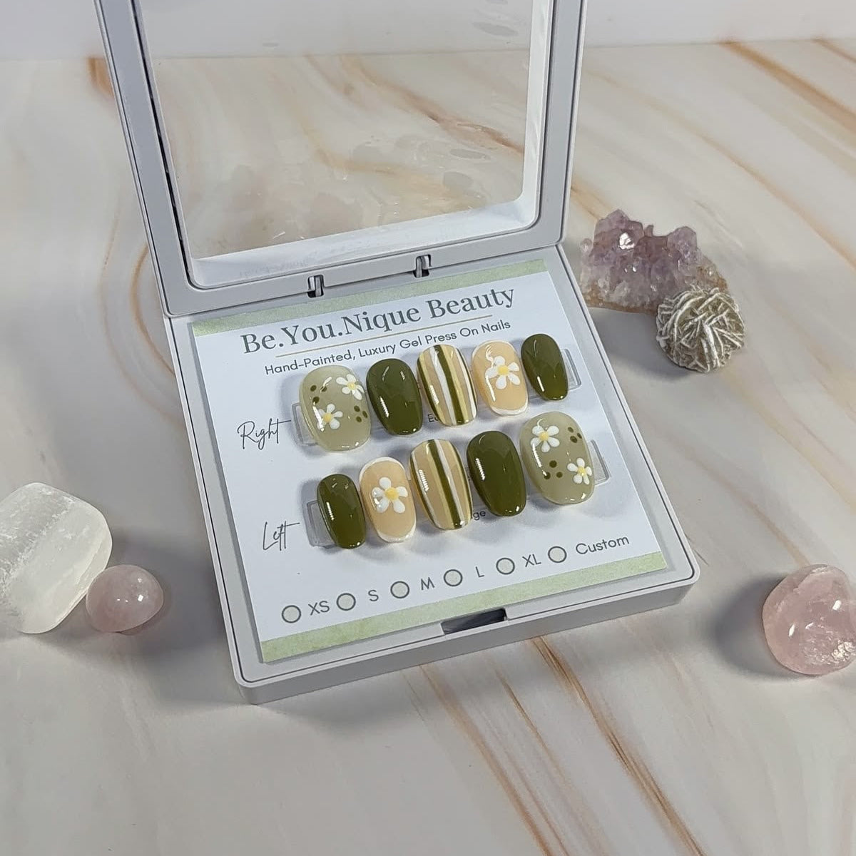 Green and white striped press ons with floral accents in a white case on a marble surface