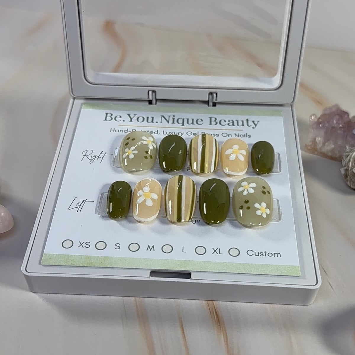 Green and white striped press ons with floral accents in a white case on a marble surface