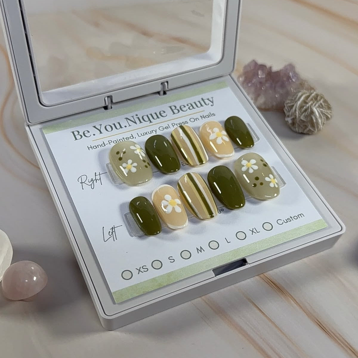 Green and white striped press ons with floral accents in a white case on a marble surface